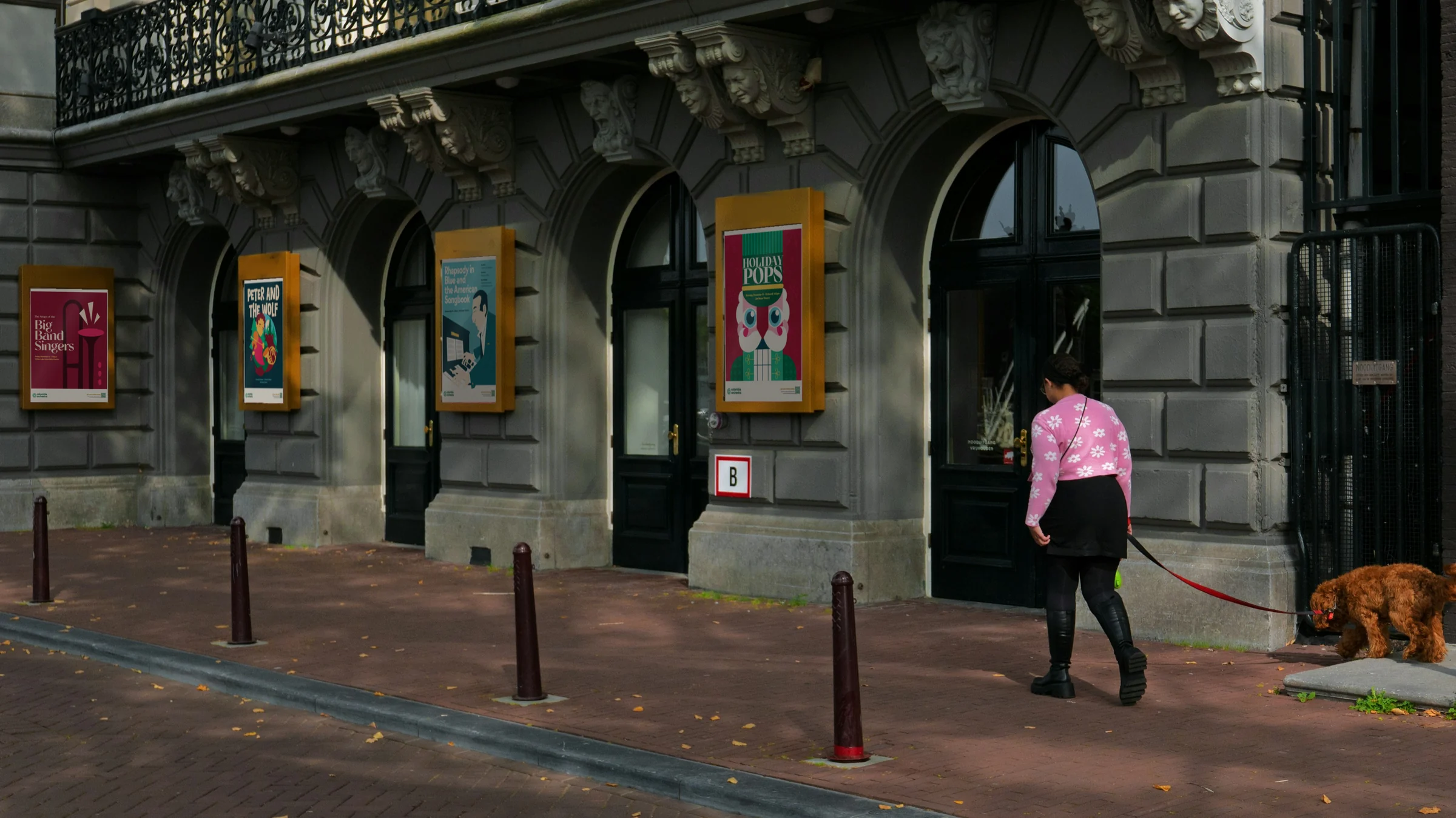 Columbia Orchestra posters in display cases outside a theatre as a woman walks her dog past